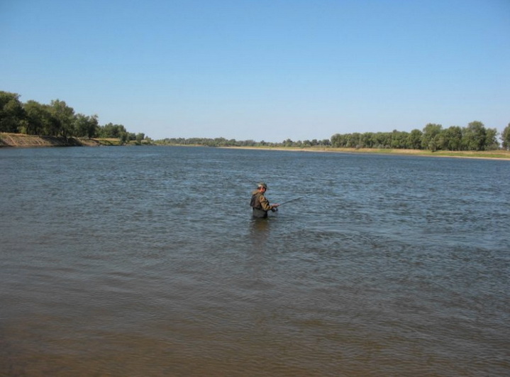 Рыболов находится в воде в реке летом